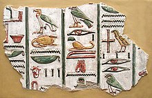 Каменный фрагмент с ярко окрашенными цветами и рельефные изображения египетских иероглифов, написанных в вертикальных колонках, на бежевом фоне