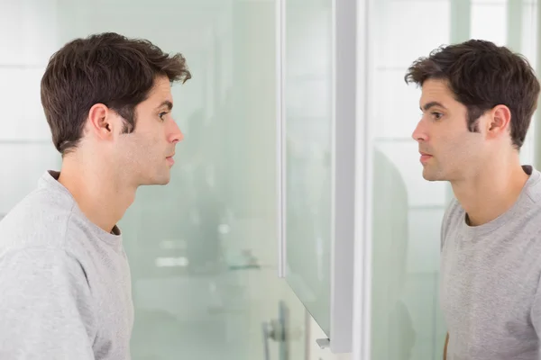 Молодой человек, улыбаясь на себя в зеркало в ванной, вид сбоку — стоковое фото