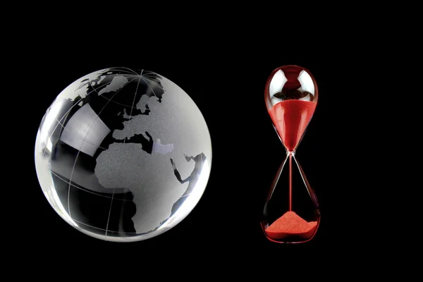 Хрустальный глобус и красным песочные часы на черном фоне. Концептуальное изображение — стоковое фото