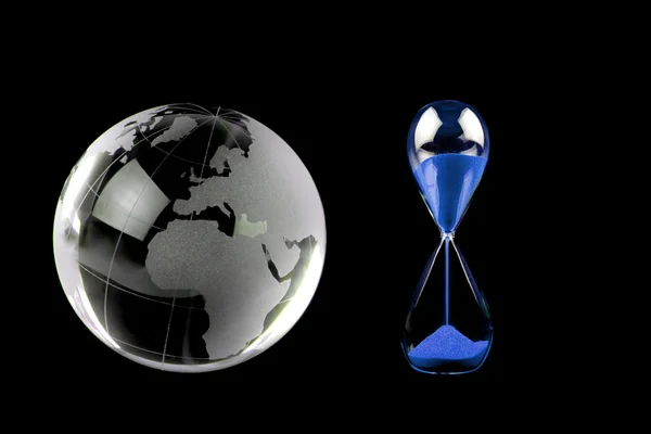 Хрустальный глобус и голубой hourglass на черном фоне — стоковое фото