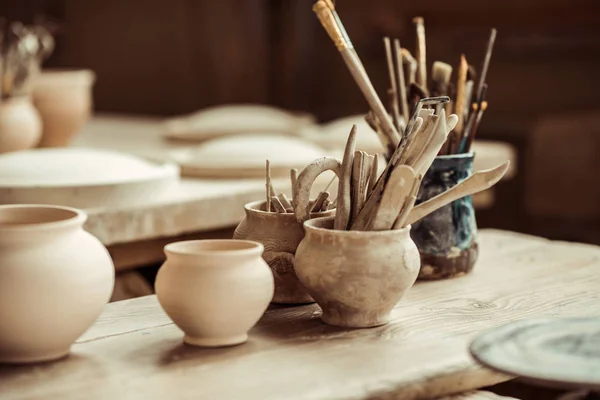 Закройте кисти с керамическими инструментами в чашках на столе — стоковое фото